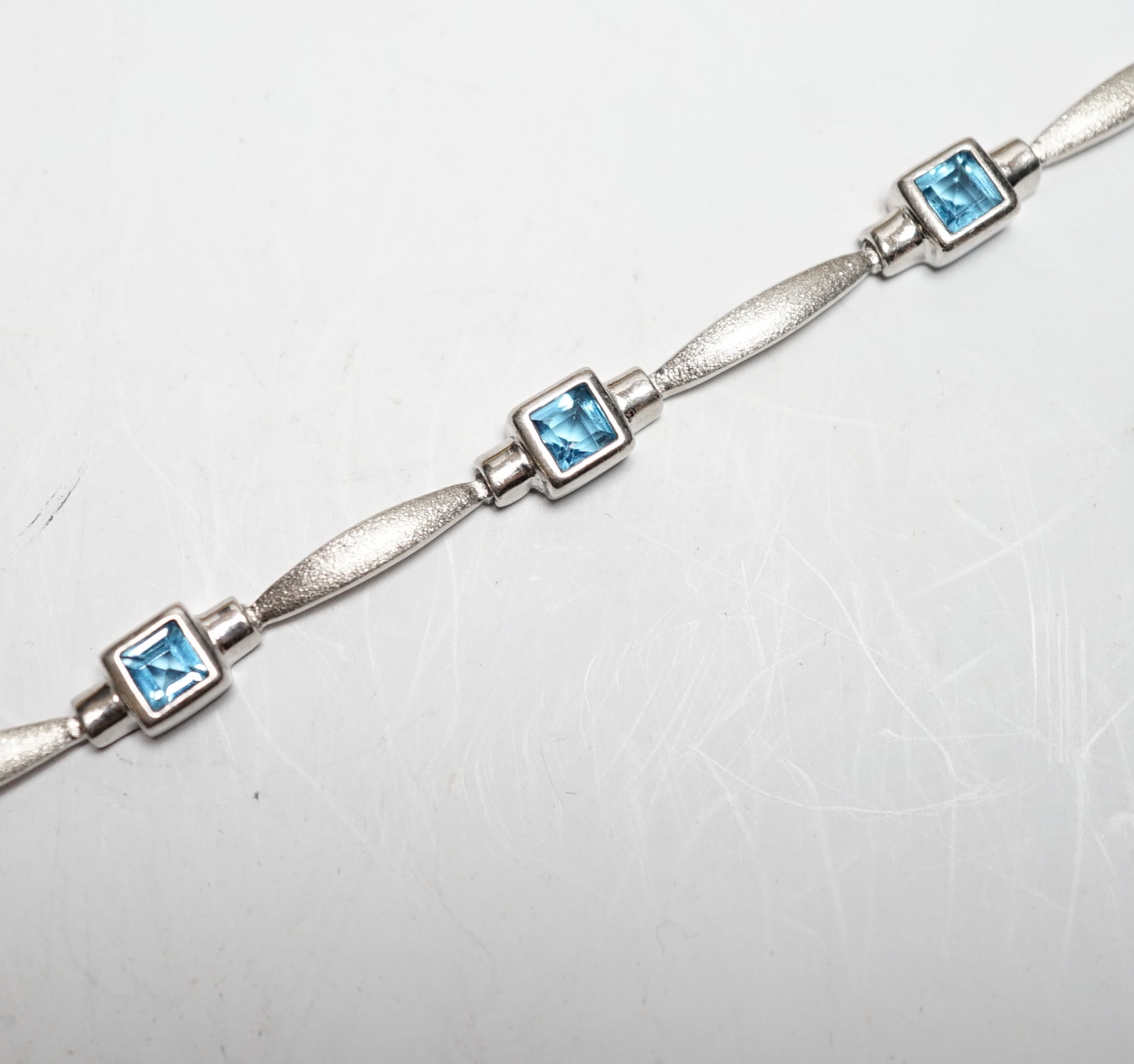 A modern brushed 9ct white gold and seven stone square cut blue topaz? set bracelet, 18cm, gross weight 8.5 grams.